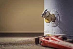 Close-up of a valve on a water heater Colorado with a small leak, as a drop of water hangs from the spout. A red pipe wrench lies on the floor—reminding you the best time to replace water heater might be now. | High 5 Plumbing, Heating & Cooling