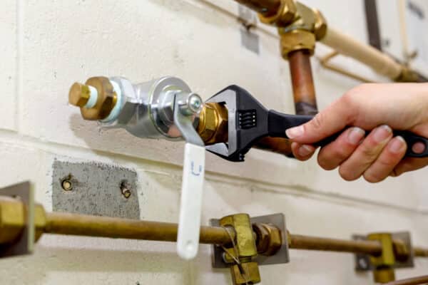 A hand holding a wrench, ready to install a vacuum breaker on an outdoor faucet. | High 5 Plumbing, Heating & Cooling